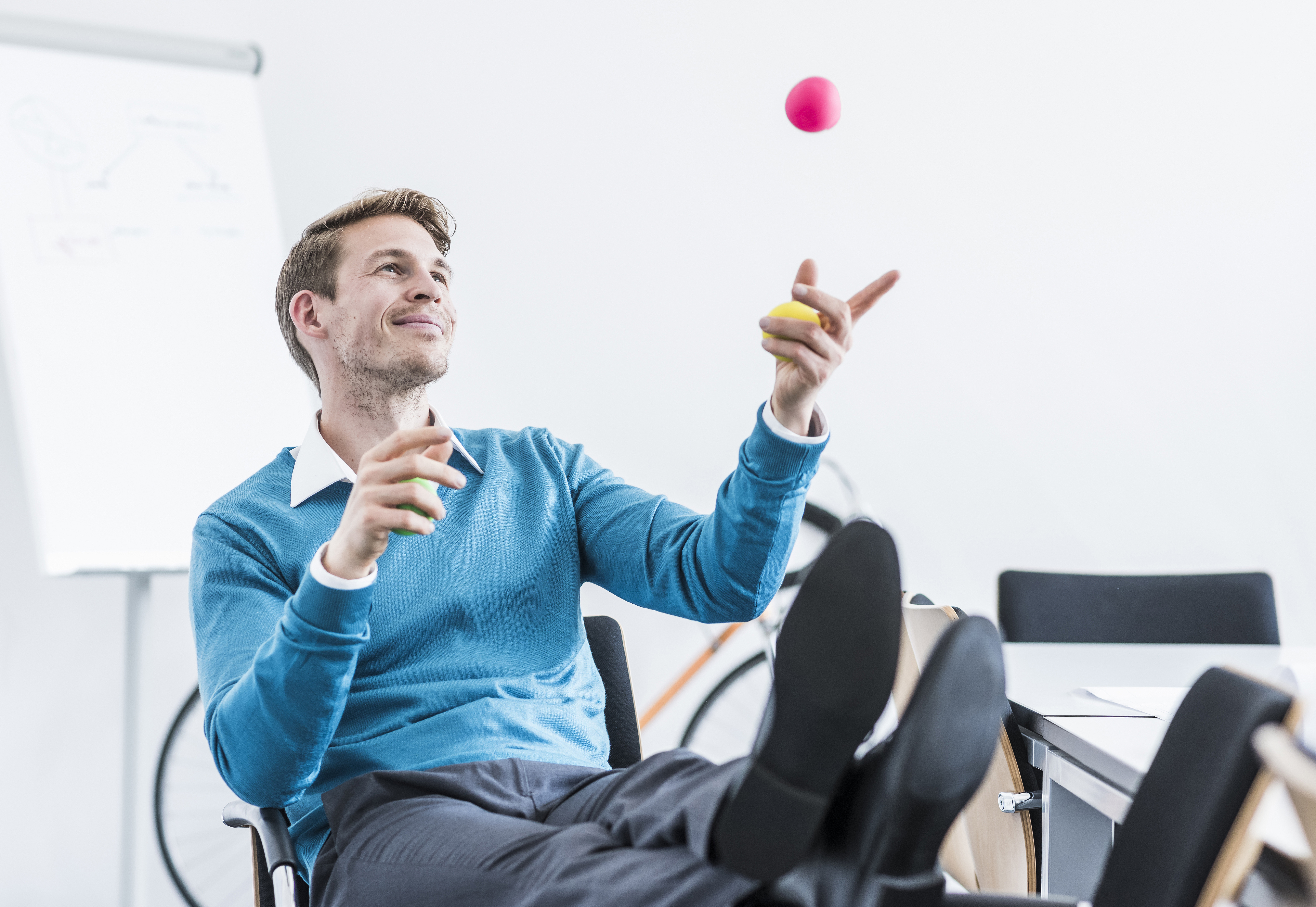 Smiling businessman juggling with balls in office